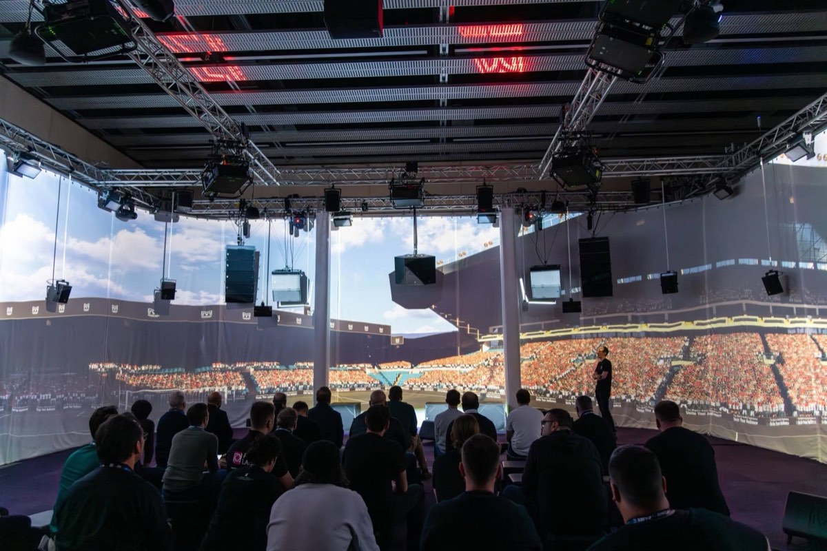 Visitors in the Martin Audio demo room at ISE watching a projection-mapped stadium scene